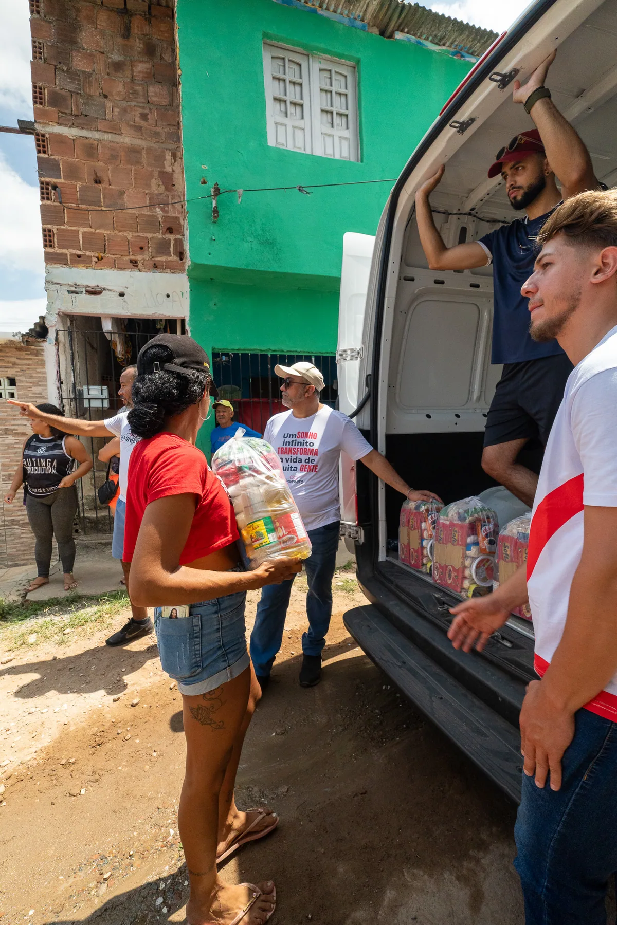 Moradores recebem itens de uma ação comunitária ao lado de um veículo